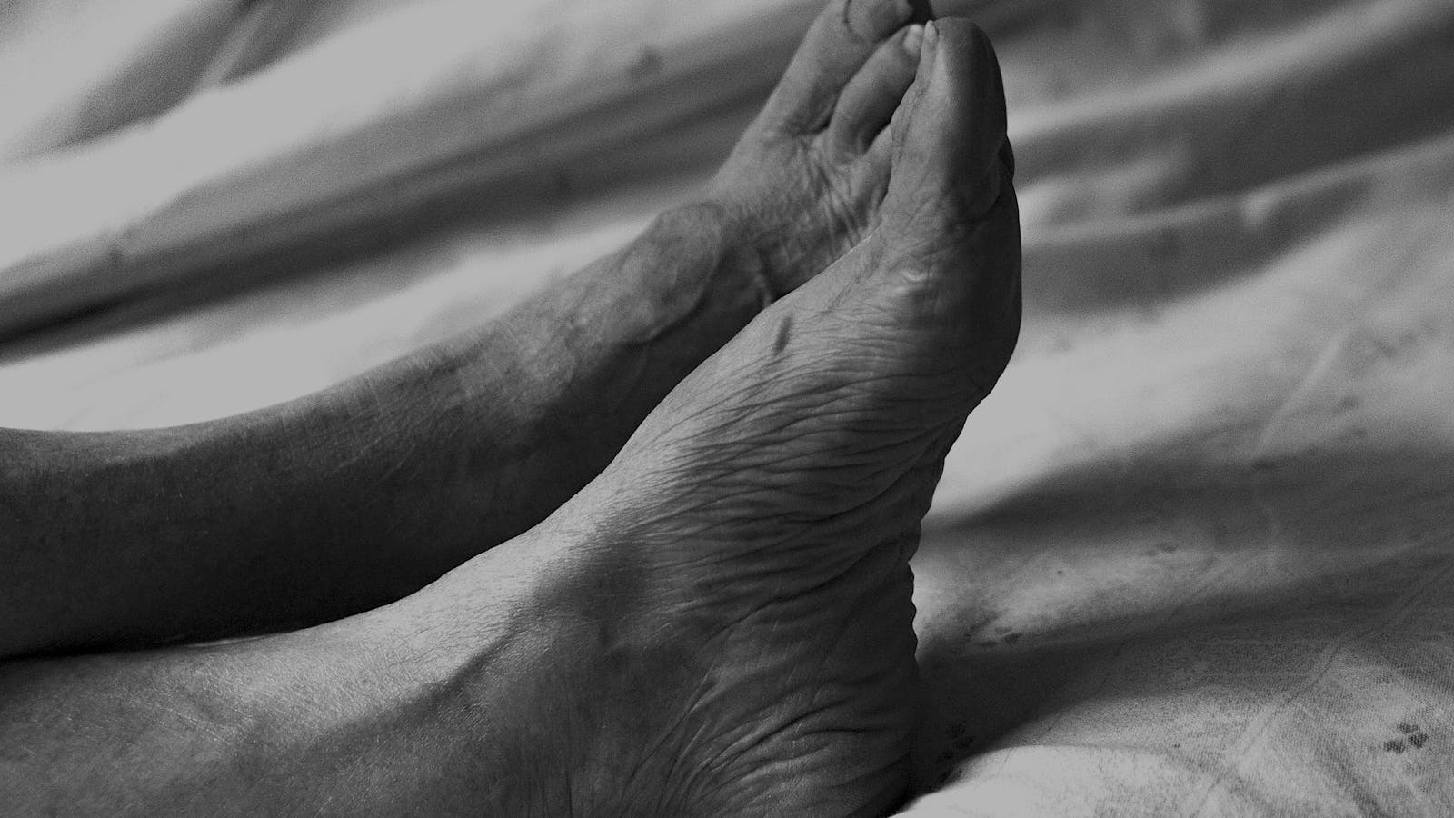 Close-up of an older adult's bare feet resting on a bed, illustrating a daily diabetic foot check.